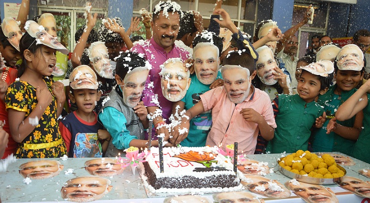 Children wearing masks of Narendra Modi cut cake to wish him best of luck